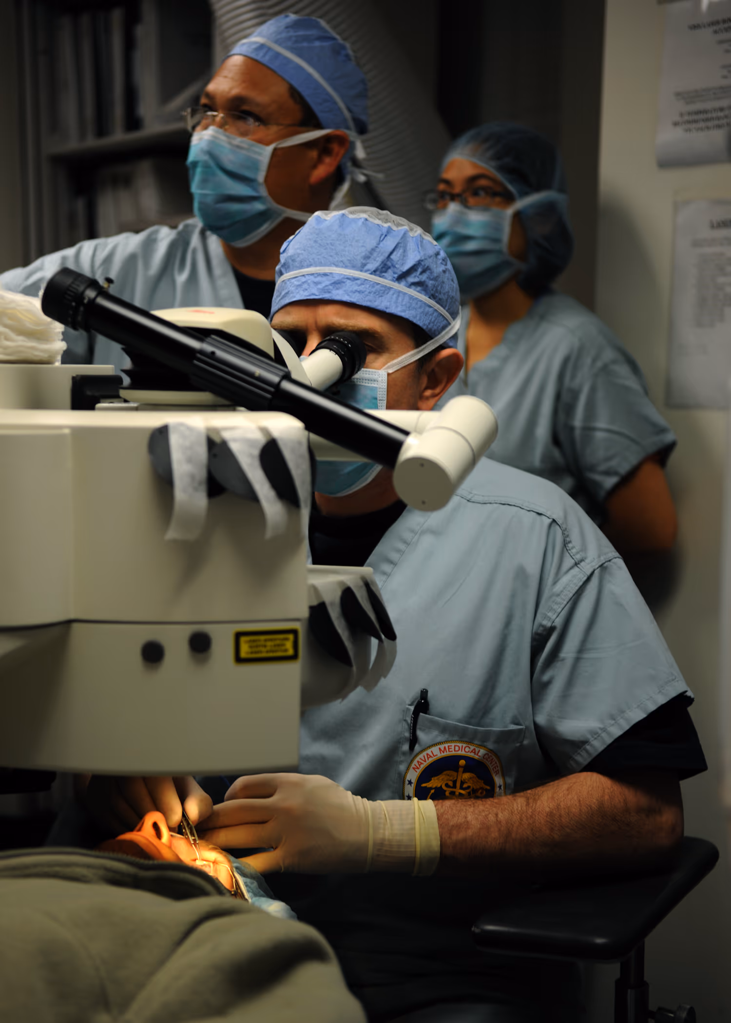 Cirurgião realizando PRK (photorefractive keratectomy) sob microscópio em centro cirúrgico refrativo. Fonte: U.S. Navy / Mass Communication Specialist 2nd Class Chad A. Bascom, via Wikimedia Commons. Domínio público.